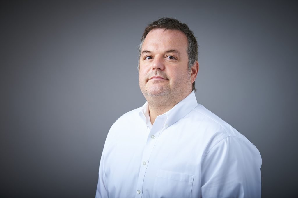 A man in white shirt standing next to wall.